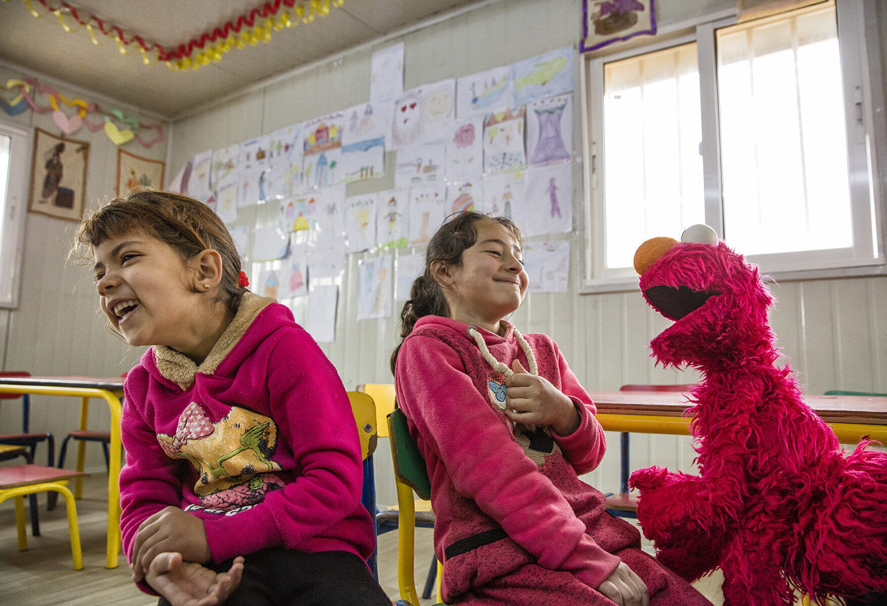 Children in the Za’atari Refugee Camp, in Jordan, play with Elmo as part of Sesame Seeds, a joint project of Sesame Workshop and the International Rescue Committee that aims to aid and nurture children who have endured extreme stress. The program is a finalist in the MacArthur Foundation’s 100&Change contest, which will award $100 million to one group.