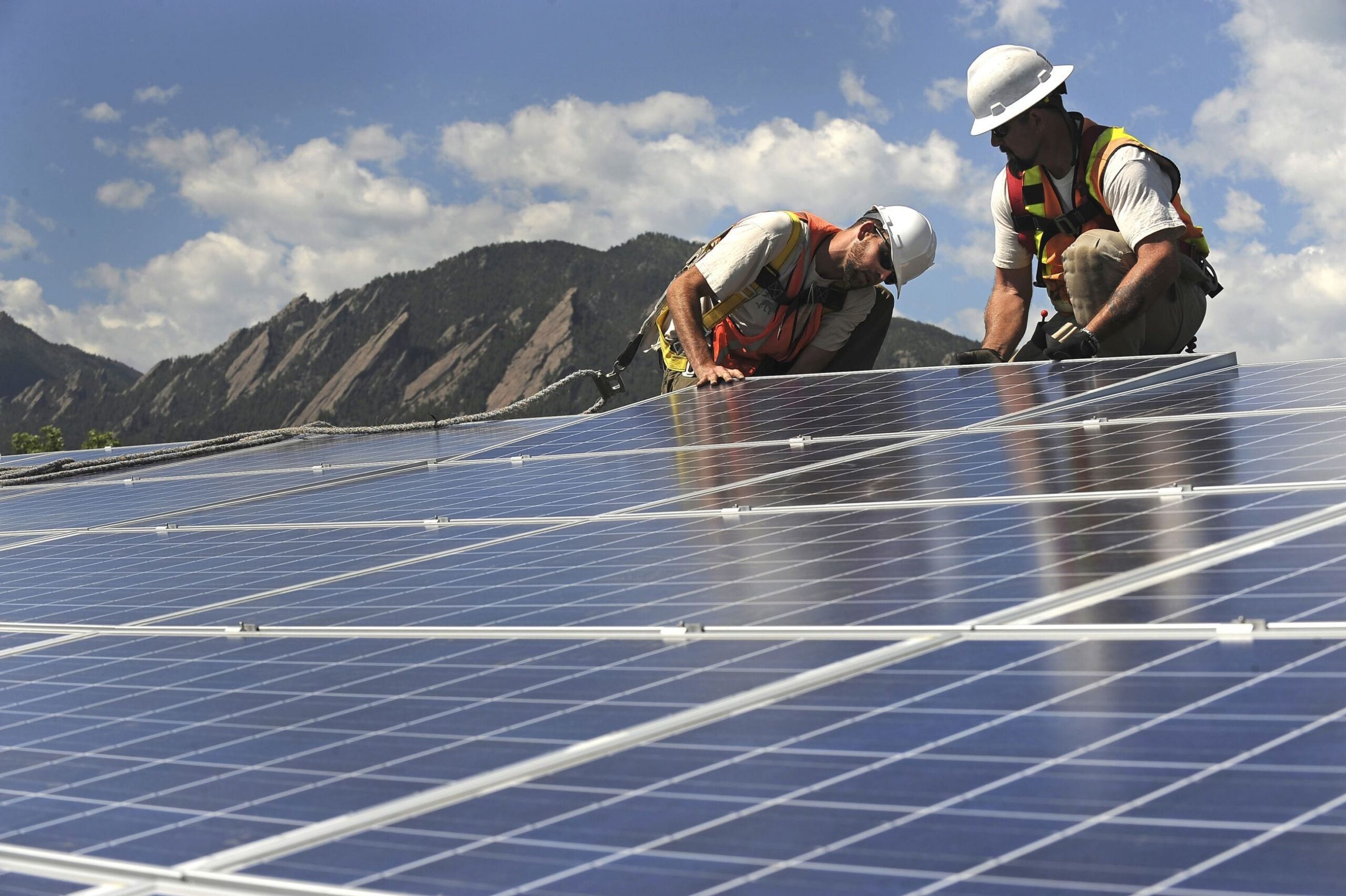 Workmen with Colorado's Xcel Energy install solar panels on a rooftop in Boulder. The city is aiming to "municipalize" electricity generation, taking it over from the private utility — one of numerous alternative strategies communities are pursuing for economic development.