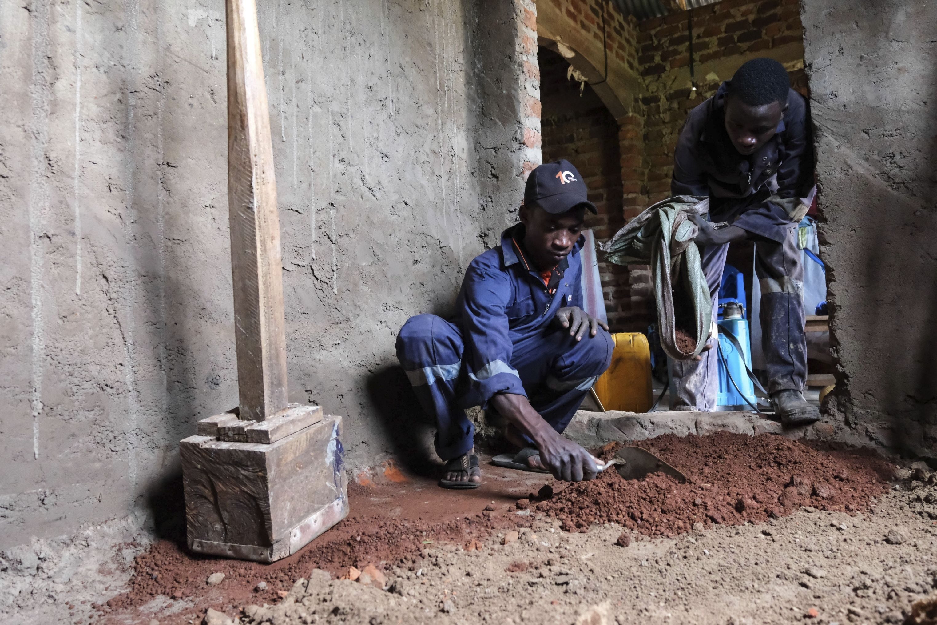 Alex Wanda, left, construction officer of EarthEnable, is helped by his colleague to prepare the ground for a clay-based earthen floor by EarthEnable on May 17, 2025, in Jinja, Uganda. (AP Photo/Hajarah Nalwadda)