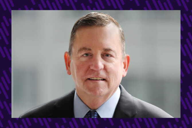 A man in a business suit and tie smiles at the camera.