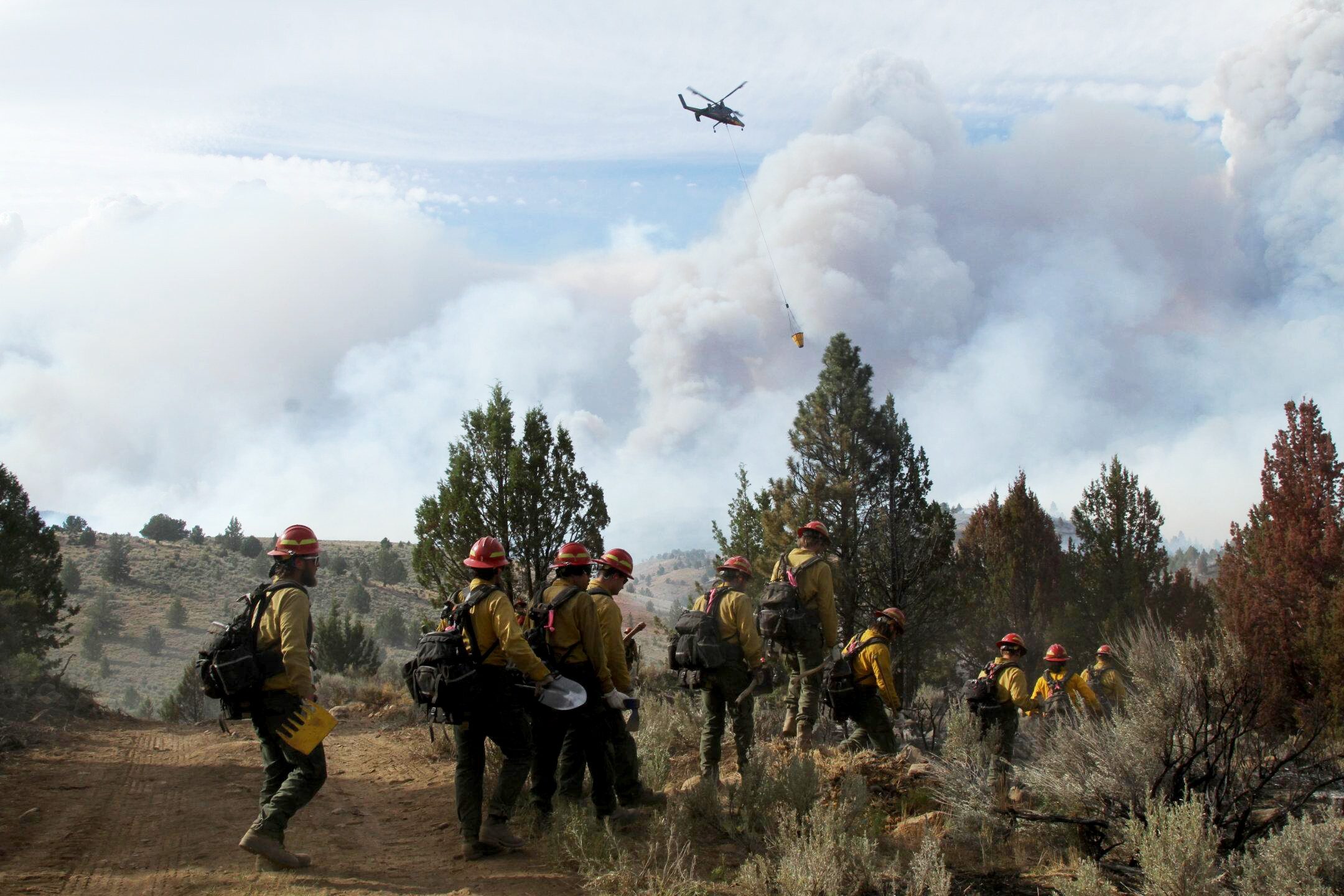 A hand crew working on the Falls Fire hikes to the fireline with the support of a helicopter on July 17, 2024.