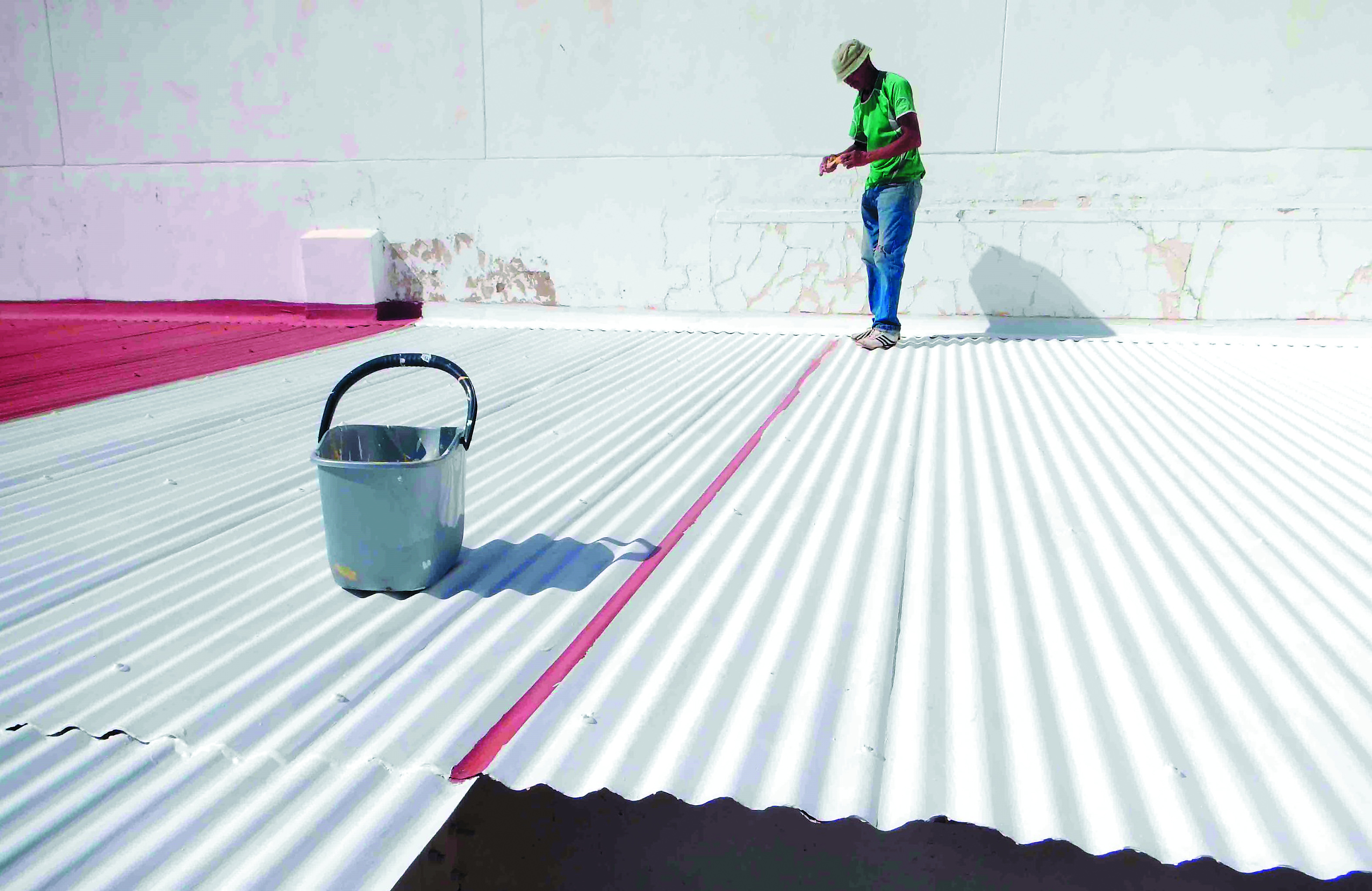 photo of a man painting a corrugated roof white