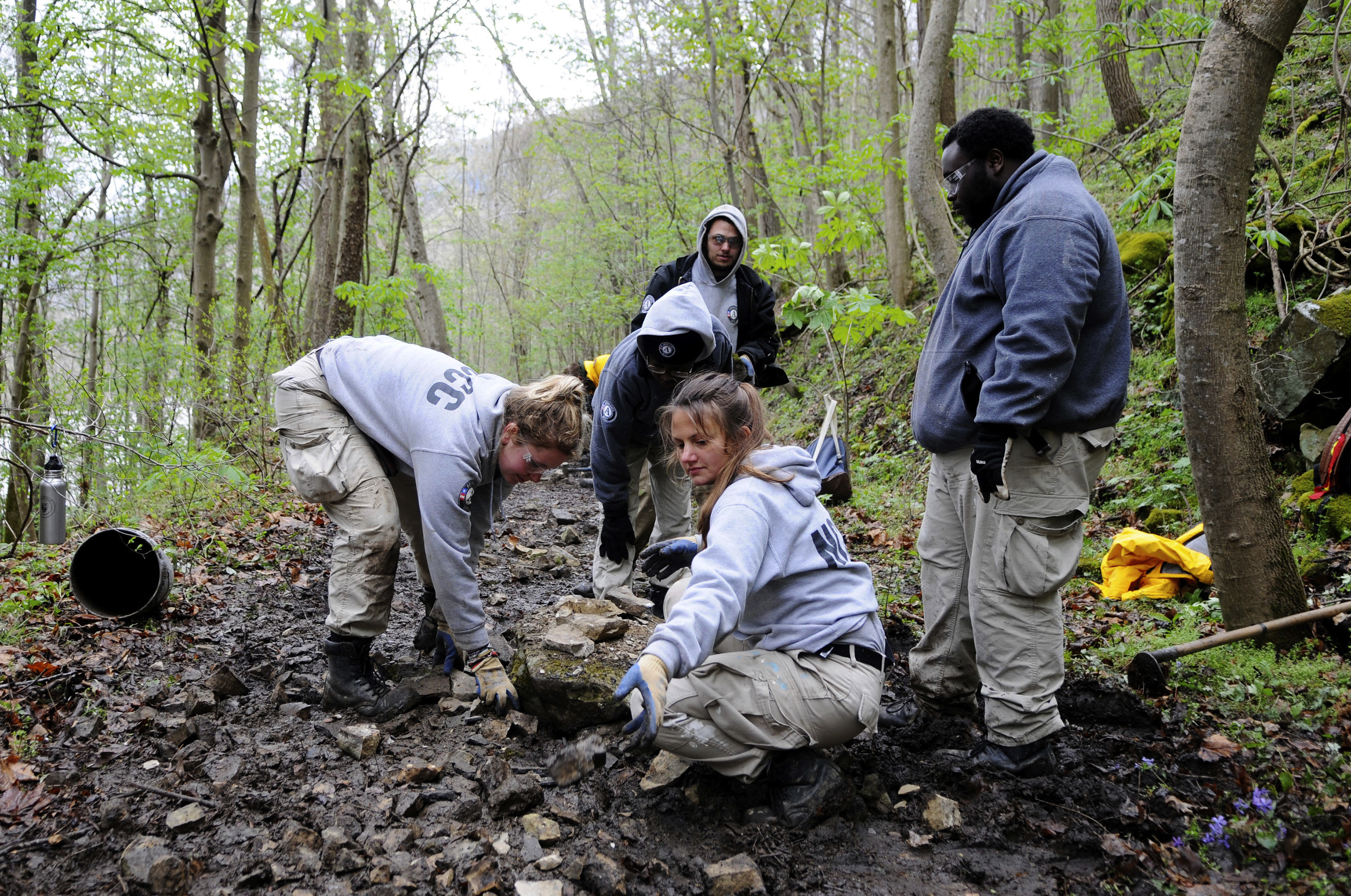 AmeriCorp members spread rocks on a muddy trail 