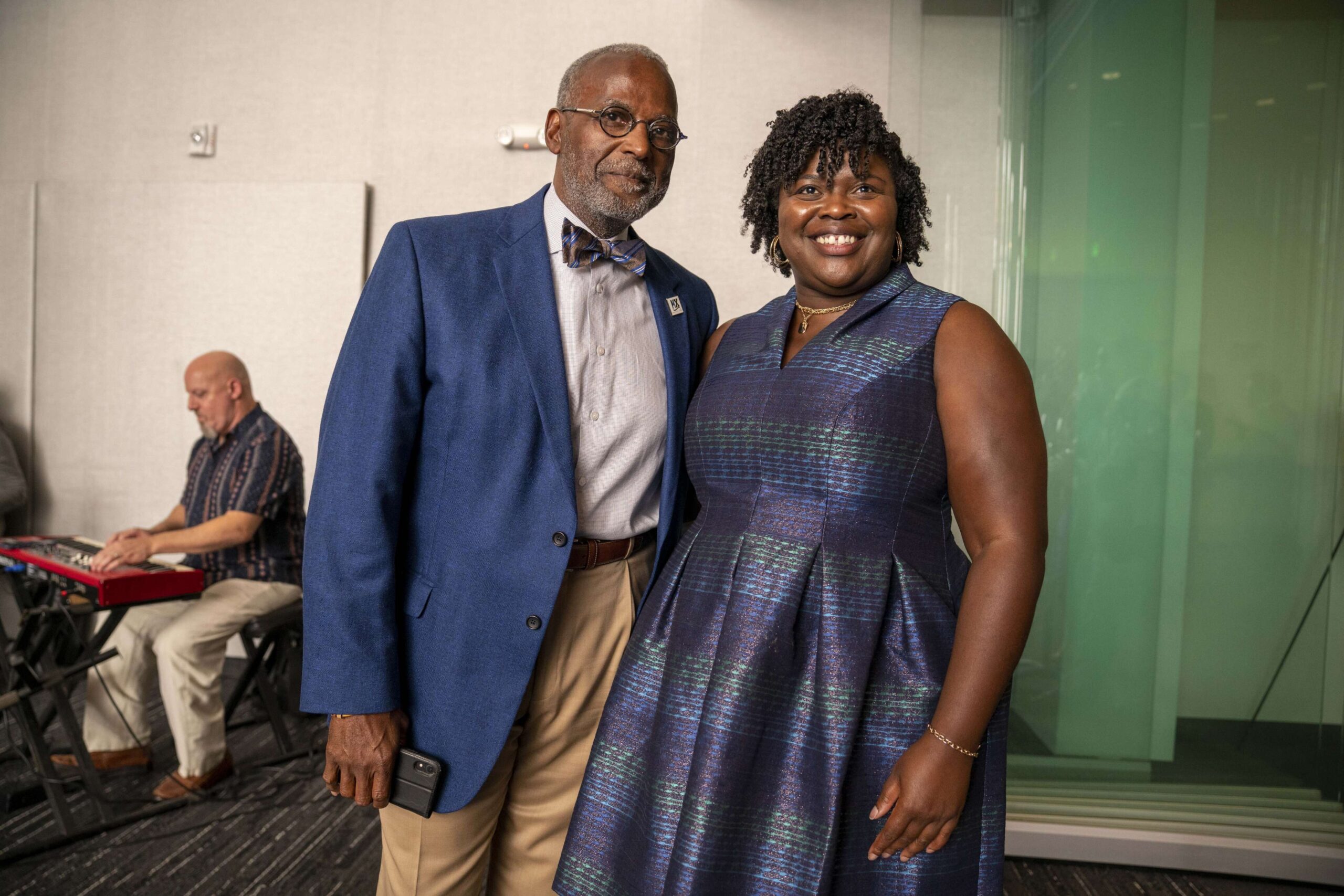 Raymond Jetson and Sherreta Harrison stand together in a room while someone plays a keyboard in the background.