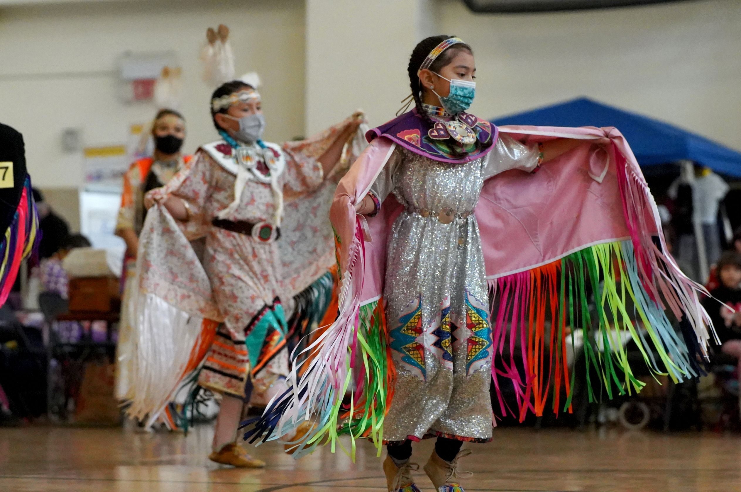 Native American children dance while wearing masks at a pow wow hosted by the American Indian Child Resource Center at the LA Escuelita Elementary School in Oakland, California, December 2021. (Garrett Rich)