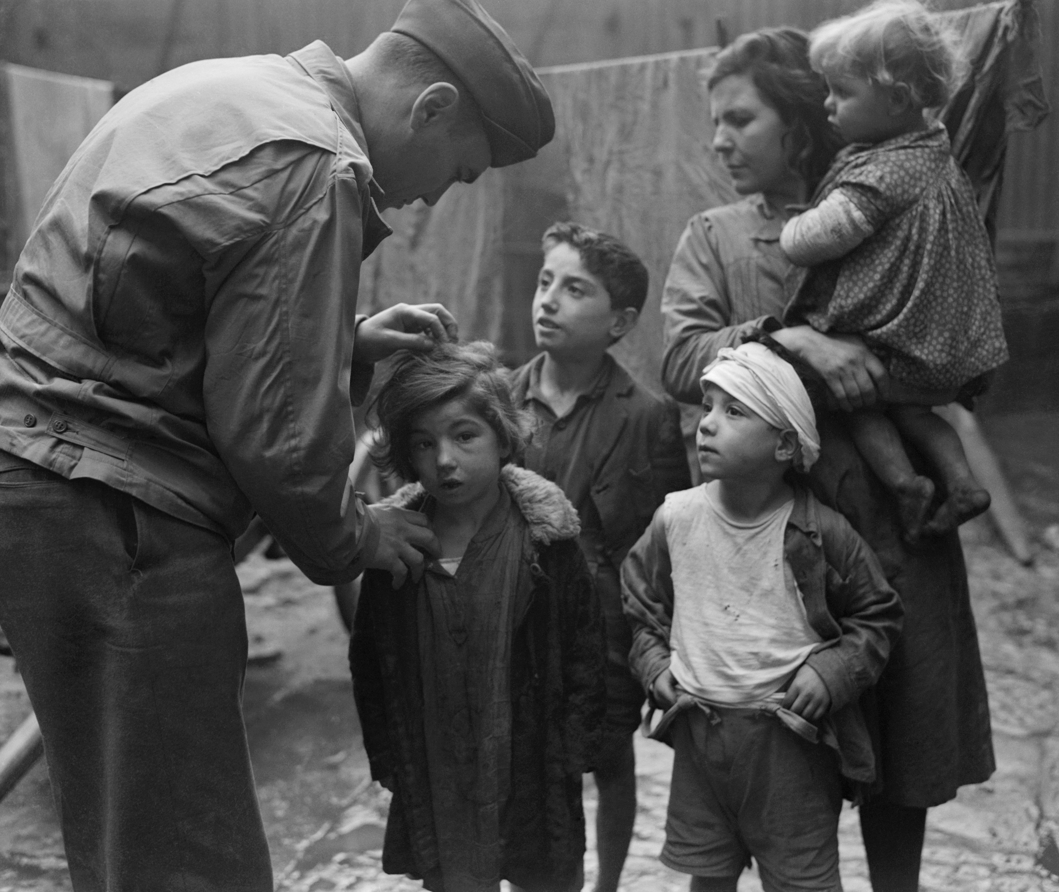 February 18, 1944 - Waat Davis, of the New York City Rockefeller Foundation, holds his little patient with one hand while he separates her hair with the other. the rest of the family, who live sin a Naples slum, watches the hunt for lice with fascinated interest as they await their turn.