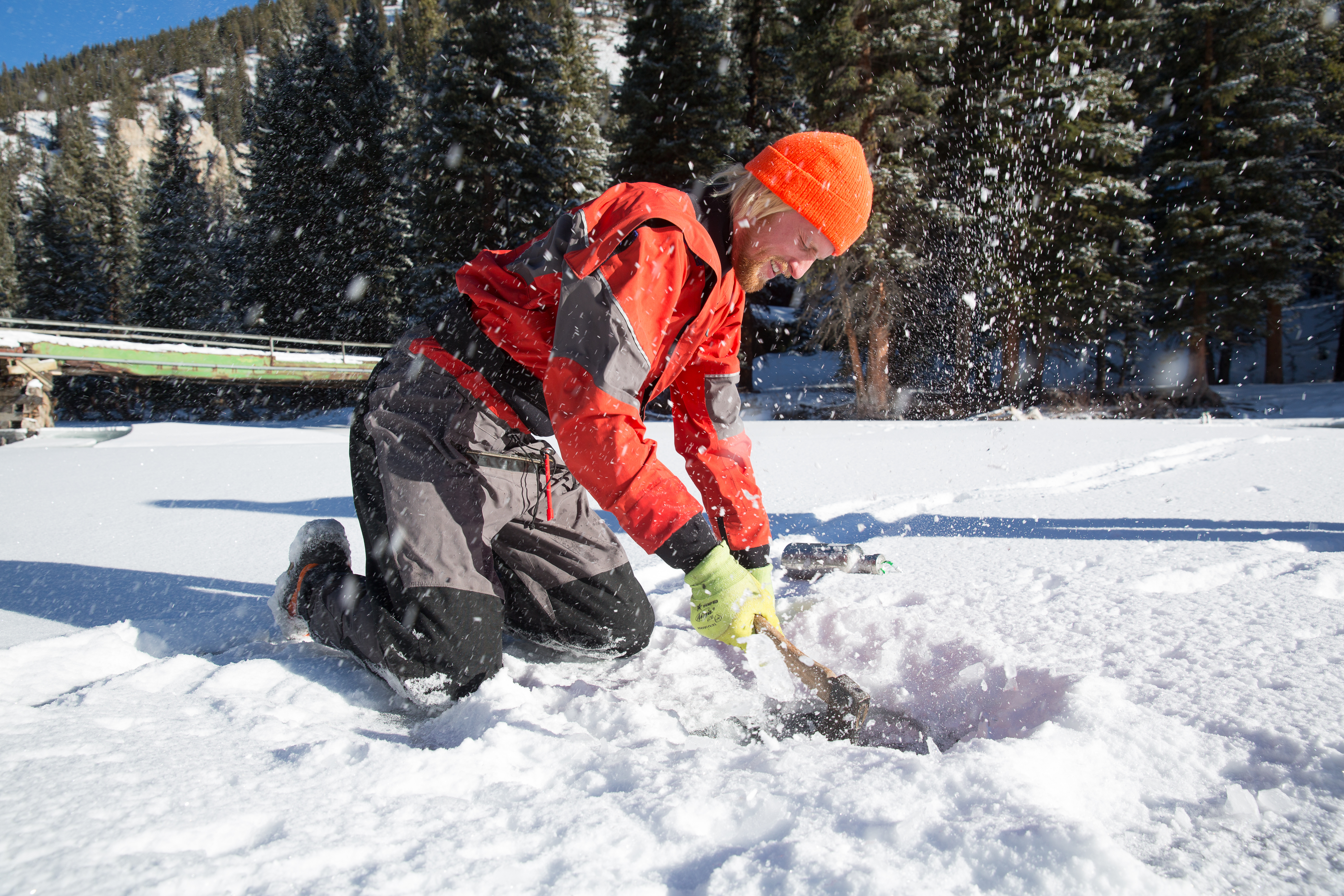 Here, a volunteer cuts through ice to collect a water sample for a project to measure microplastic pollution in Montana’s Gallatin River.