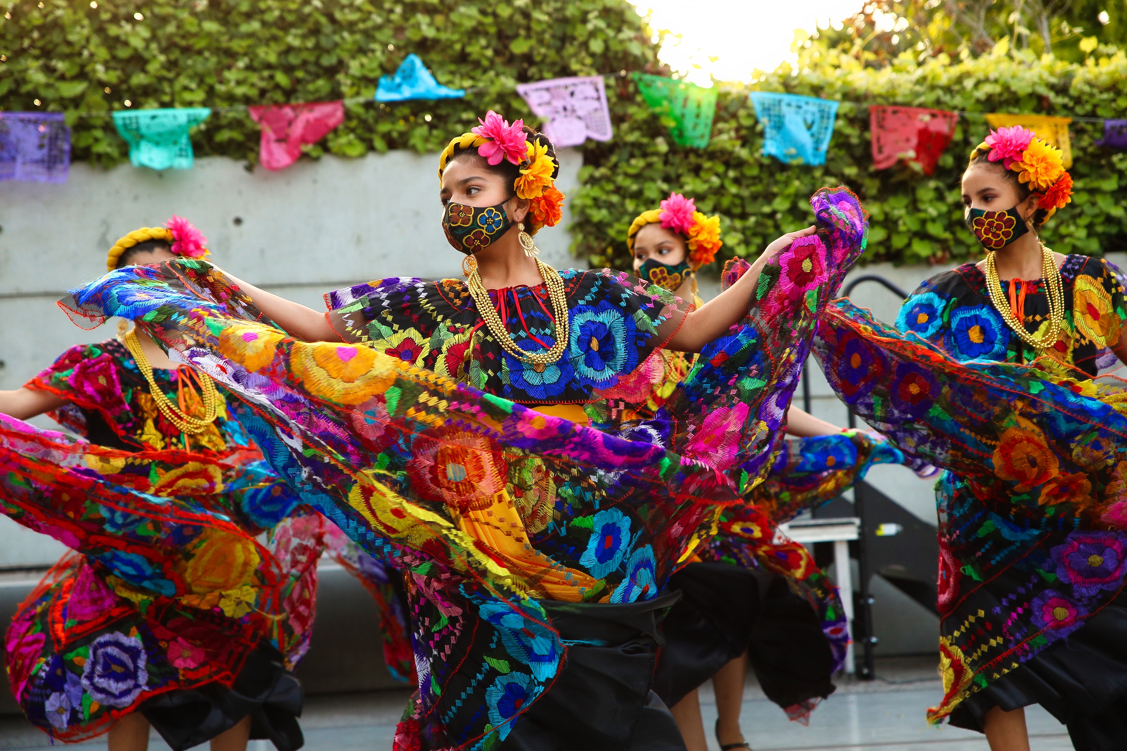 Four dancers in colorful costumes are seen performing on an outdoor patio.