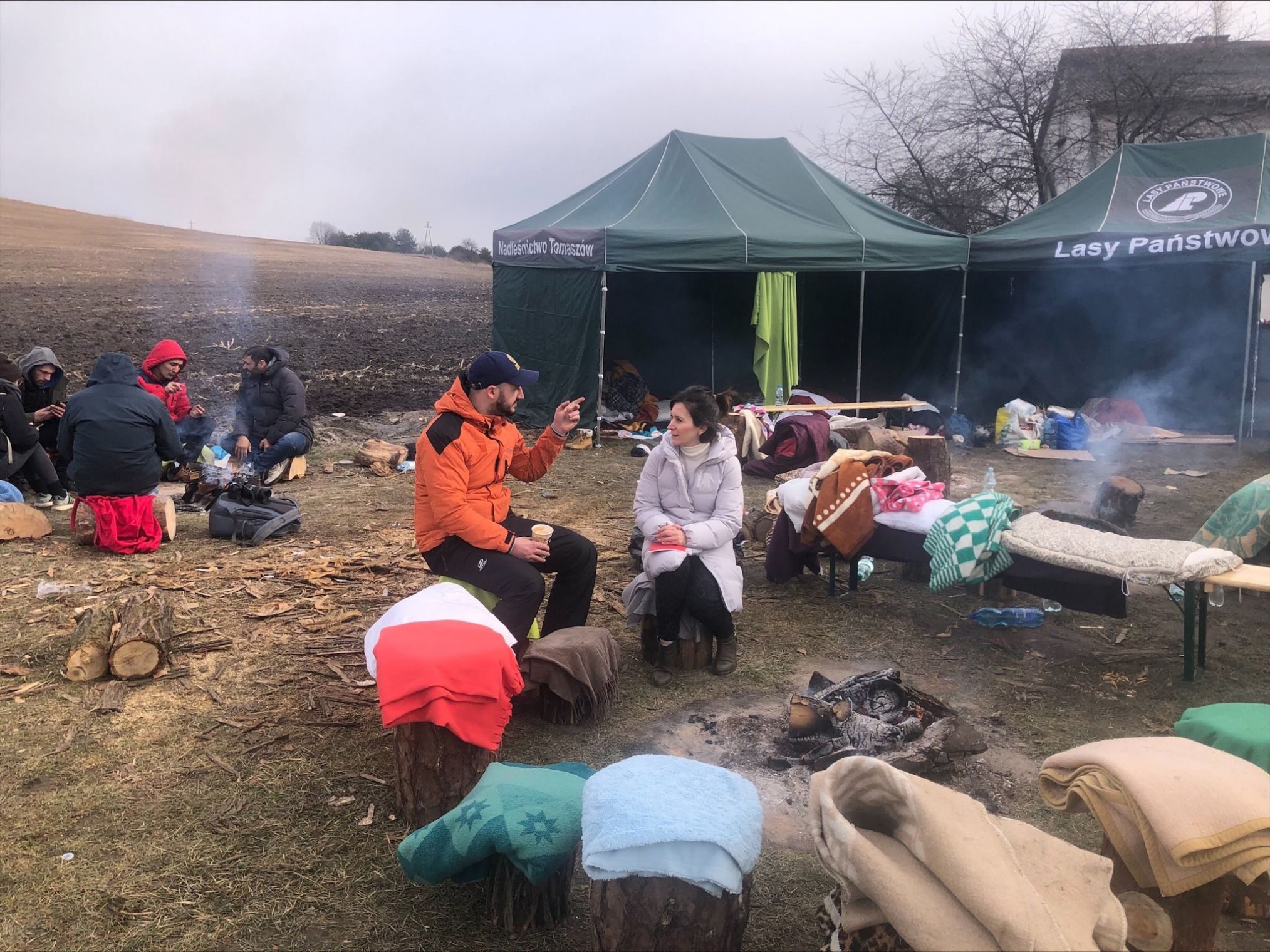 Simge Memisoglu (International Medical Corps country rep in Poland, wearing light pink coat) talking to people who have fled Ukraine at a reception center along the Polish border with Ukraine. The man in orange was waiting for his mother to cross into Poland from Ukraine.