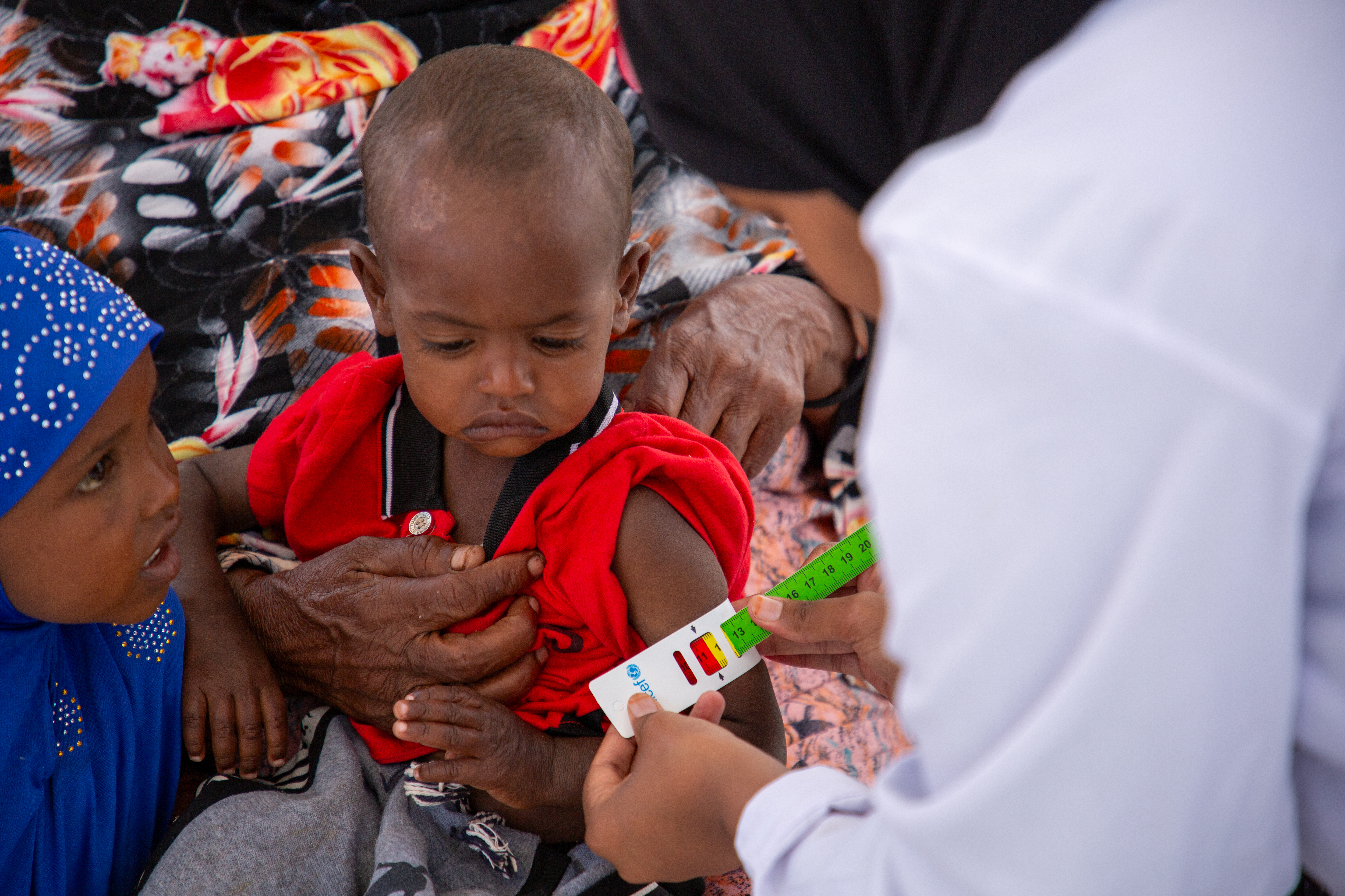 A Save the Children nurse checks Abdi's arm with a MUAC tape to determine his nutrition level. The family struggles with severe poverty and drought, and they have no stable source of food or milk. With no access to proper nutrients, Abdi’s health deteriorated significantly. A local health worker connected the family to a Save the Children health centre where Abdi received the necessary treatment, leading to a gradual improvement in his condition.