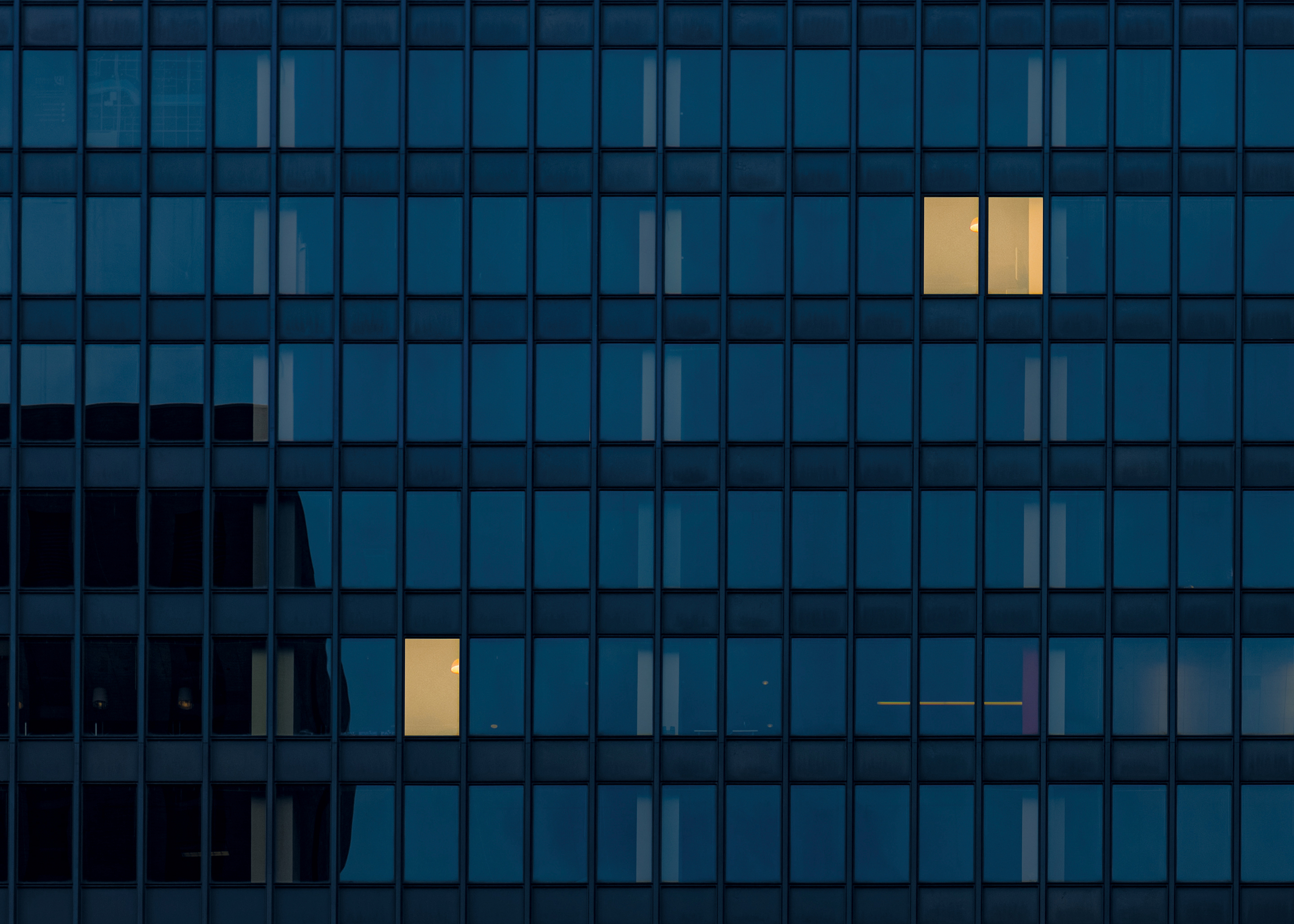 Photo illustration showing a skyscraper at twilight. Only a few office lights are on.