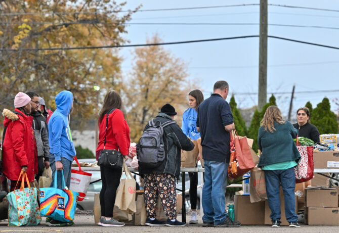 People receiving groceries and supplies from tables at an outdoor community food distribution event.