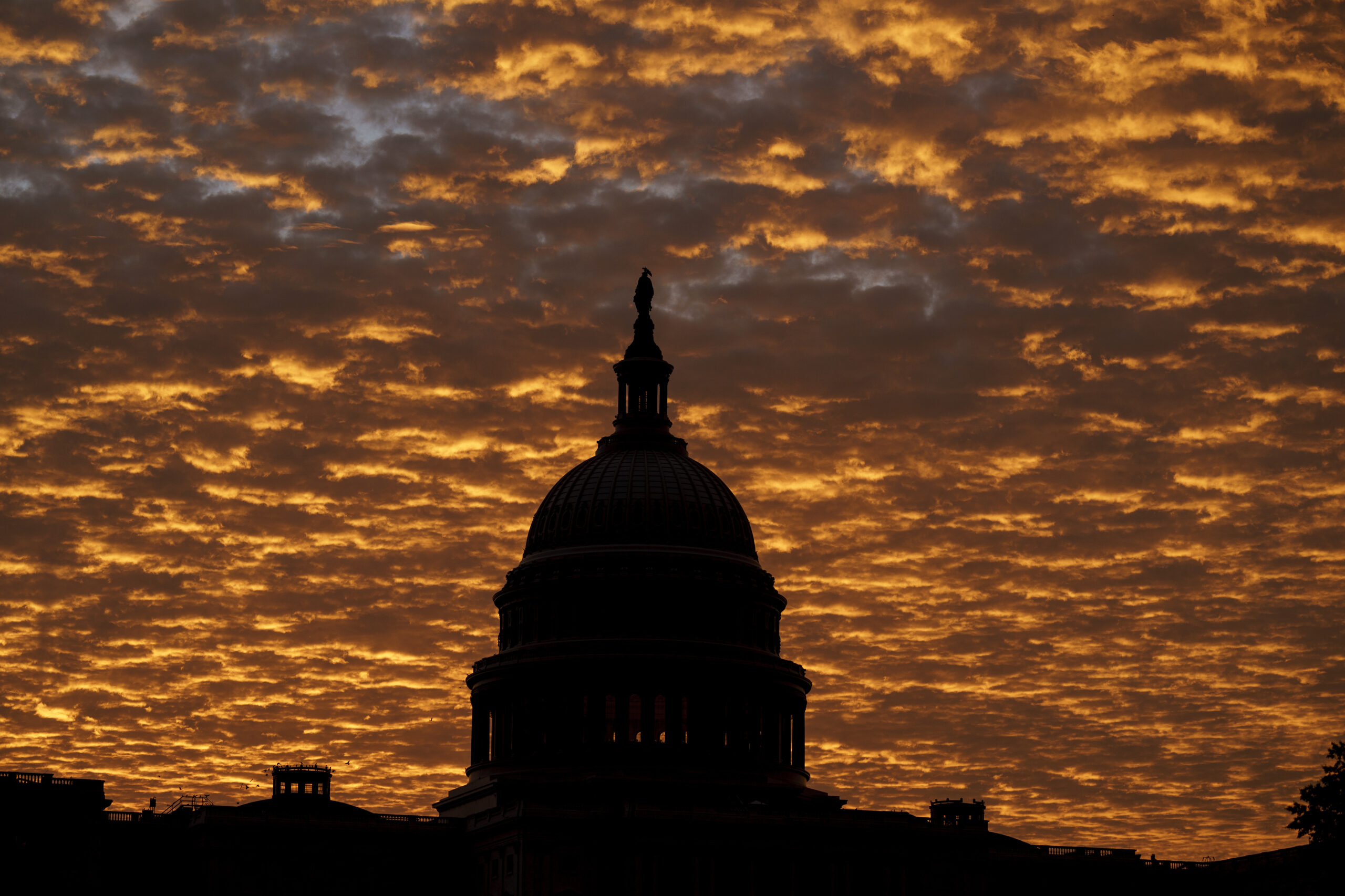 Silhouette of the U.S. Capitol Building Dome against a dramatic orange-hued sky filled with glowing clouds at sunrise.