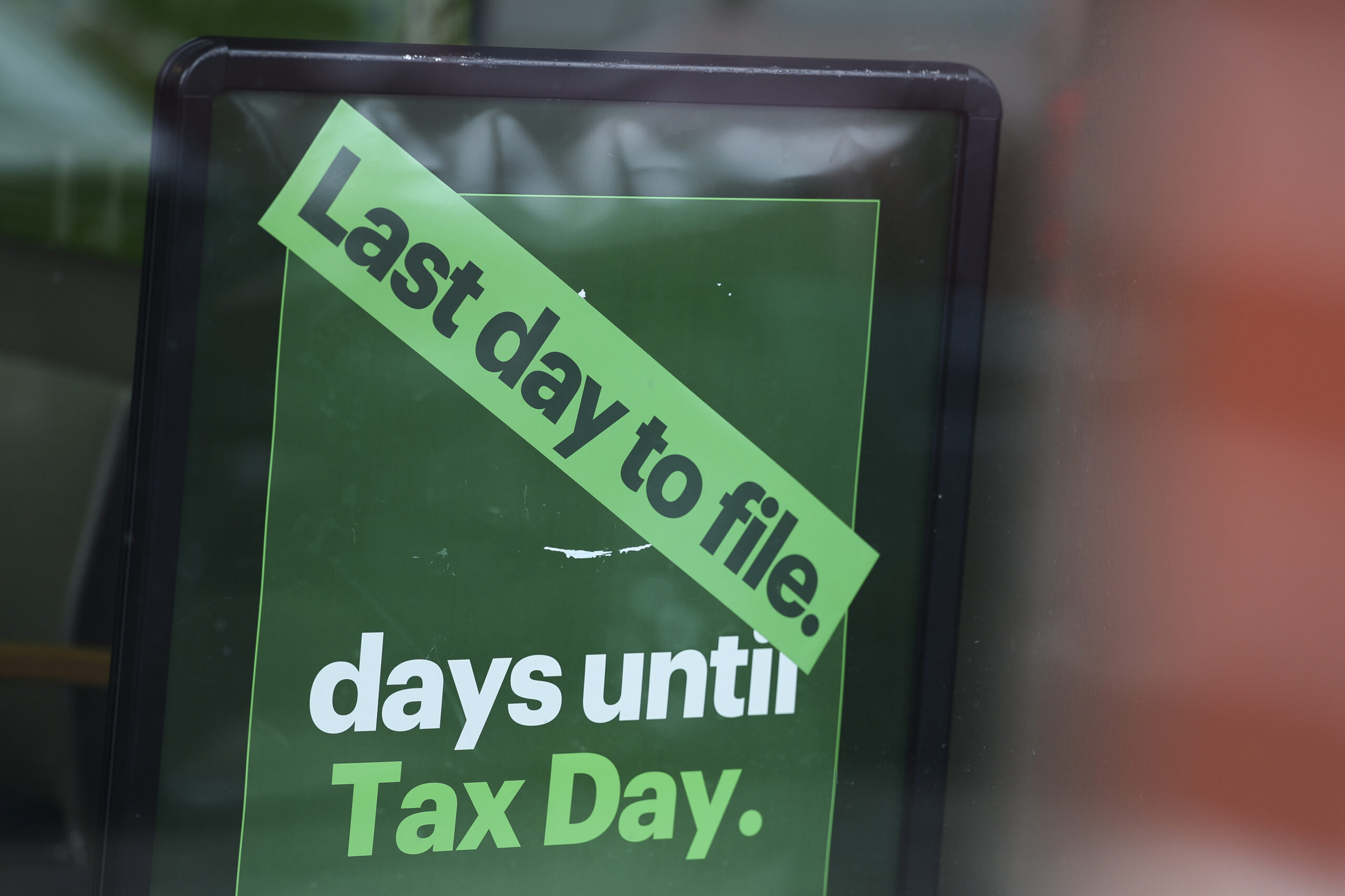 A close-up of a green sign with a diagonal bright green strip reading 'Last day to file.' Below it, white text says 'days until' and green text says 'Tax Day,' indicating an urgent tax deadline.