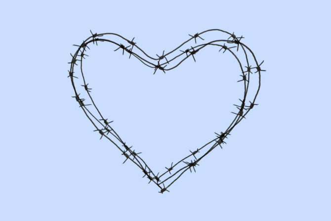 A heart shape made of dark barbed wire, with sharp barbs, set against a plain light blue background.