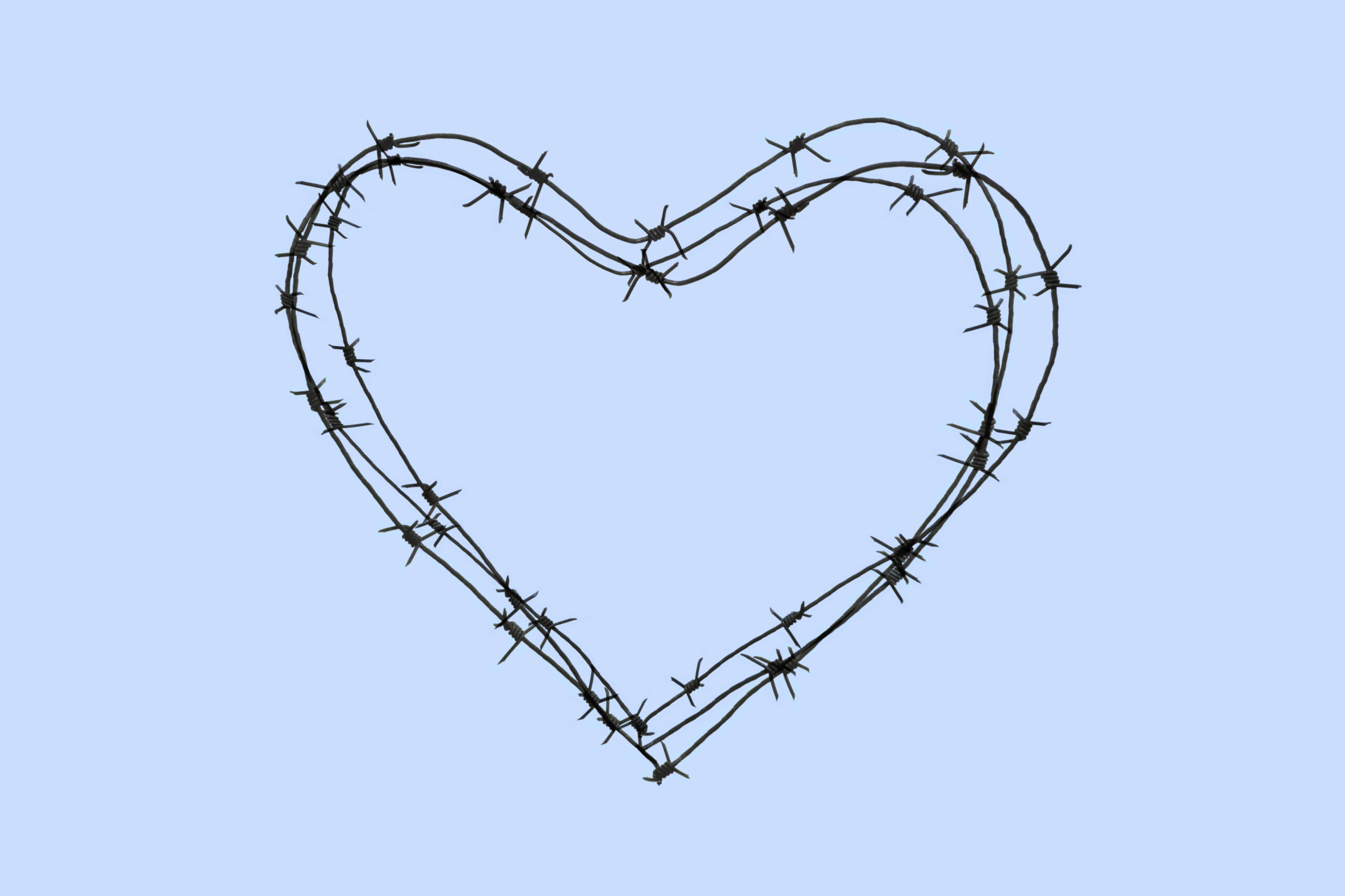 A heart shape made of dark barbed wire, with sharp barbs, set against a plain light blue background.