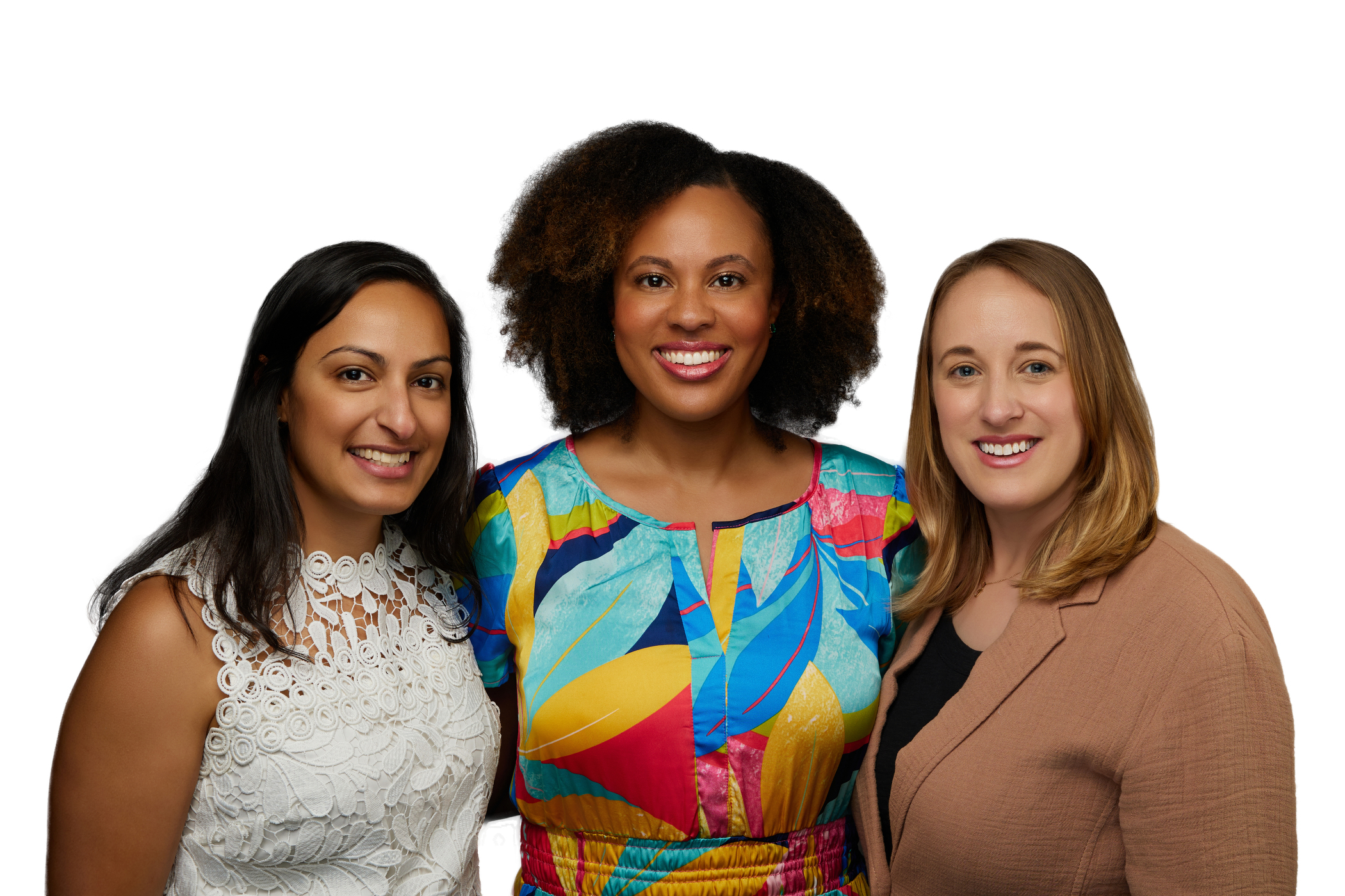 Three diverse women smiling at the camera: one with dark hair in a white lace top, one with curly hair in a colorful dress, and one with light brown hair in a tan blazer.
